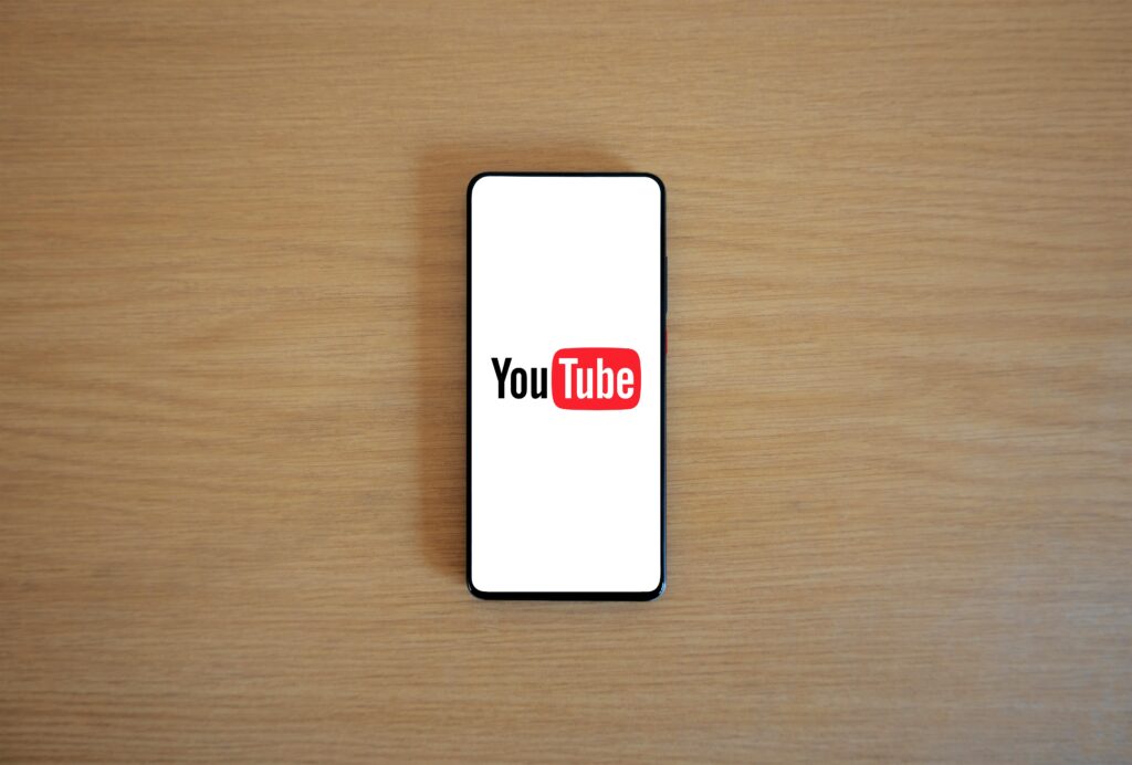 Top view of smartphone displaying YouTube logo on a wooden surface, showcasing modern technology.